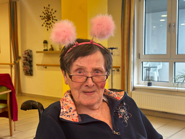 Ältere Frau mit Brille und einem lustigen Stirnband mit pinken Pompons.