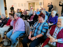Ältere Menschen sitzen in einem Saal und hören aufmerksam zu.