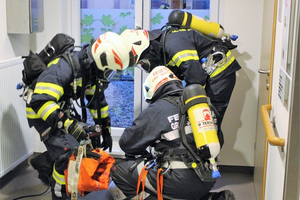 Feuerwehrleute überprüfen Ausrüstung in einem Flur nahe einer Tür.