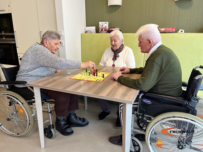 Drei Senioren spielen gemeinsam ein Brettspiel an einem Tisch.