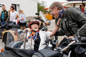 Eine fröhliche ältere Frau sitzt im Motorrad und unterhält sich mit einem Mann.