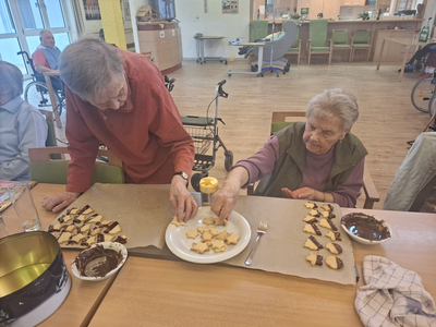 Zwei Senioren dekorieren Plätzchen in einem Gemeinschaftsraum.