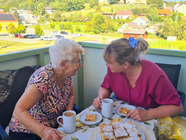 Zwei Frauen genießen Kaffee und Kuchen auf einem Balkon mit schöner Landschaft.