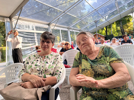 Zwei Frauen sitzen in Stühlen unter einem Zelt und schauen zum Publikum.