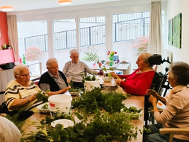 Ältere Menschen sitzen am Tisch und verarbeiten frische Kräuter zusammen.