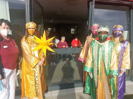 Sternsinger und Betreuer vor einer Einrichtung, drinnen sitzen ältere Menschen.