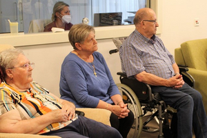 Ältere Menschen sitzen in einem Raum und hören aufmerksam zu.