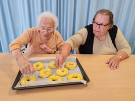 Zwei ältere Frauen bestreuen frische Teigkringel auf einem Backblech.