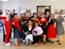 Eine Gruppe von Frauen in festlicher Kleidung, die Platten präsentieren und fröhlich posieren.
