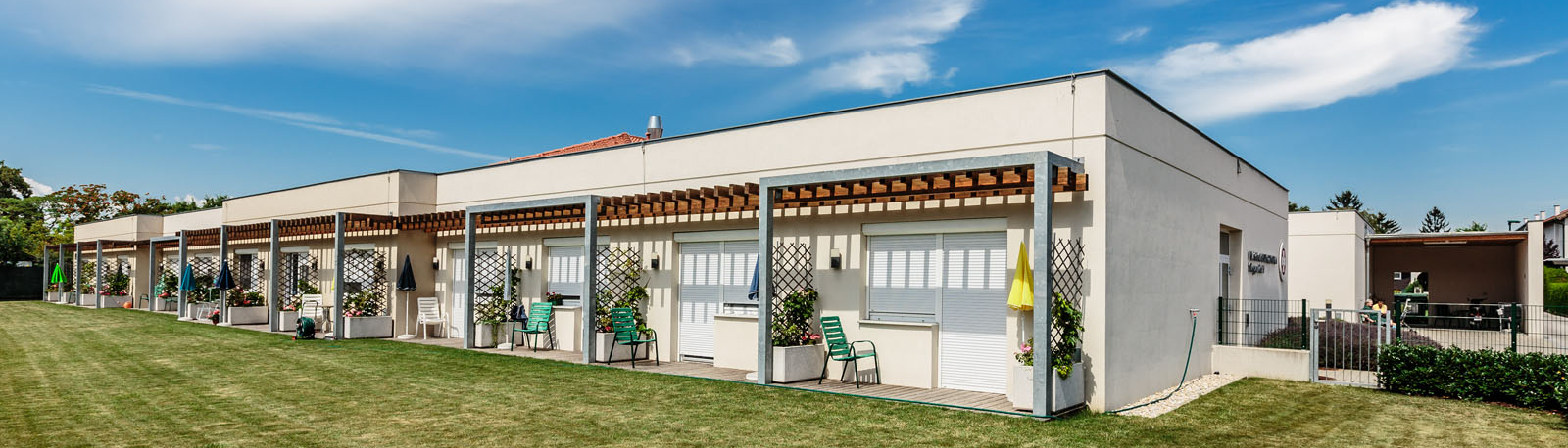 Moderne Gebäudefront mit überdachten Terrassen und grünem Rasen.