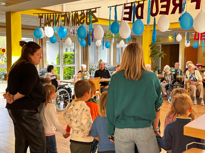 Kinder stehen mit Erwachsenen zusammen und singen für ältere Menschen in einem Gemeinschaftsraum.