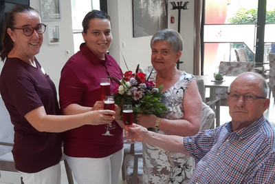Vier Personen stoßen mit Gläsern an, eine hält einen Blumenstrauß.