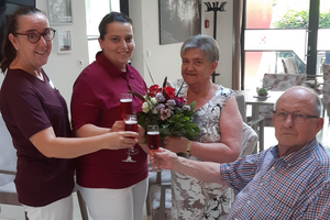 Vier Personen stoßen mit Gläsern an, eine hält einen Blumenstrauß.