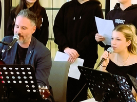Mann mit Gitarre und Frau am Mikrofon während eines Auftritts.