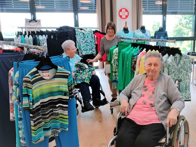 Drei Frauen in einem Bekleidungsgeschäft mit bunter Kleidung in einem hellen Raum.
