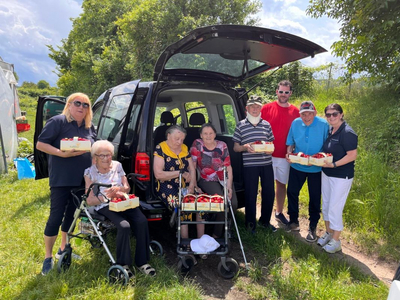 Eine Gruppe von Menschen hält Erdbeeren vor einem Auto in der Natur.