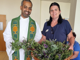 Ein Mann in priesterlicher Kleidung und eine Frau halten einen Korb mit Kräutern.