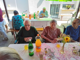 Senioren sitzen an einem Tisch mit Getränken und Dekoration im Freien.