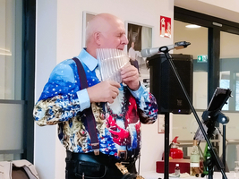 Ein Mann spielt Panflöte und singt, trägt ein auffälliges, festliches Hemd.