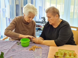 Zwei Frauen basteln gemeinsam mit Pflanzenmaterial in einem hellen Raum.