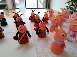 Bunte Figuren aus Blumentöpfen, gestaltet als Marienkäfer und Schweine, stehen auf einem Tisch.