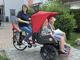 Eine Betreuerin fährt zwei ältere Damen in einem Rikschawagen.