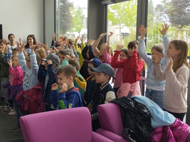 Eine Gruppe von Kindern hebt begeistert die Hände in einem Raum.