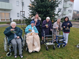Sechs Frauen in Rollstühlen stehen vor einem Weihnachtsbaum und halten Dekorationen.