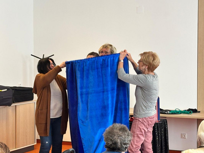 Vier Frauen halten gemeinsam einen blauen Vorhang hoch.