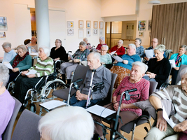 Eine Gruppe älterer Menschen sitzt, einige in Rollstühlen, und hält Liederblätter.