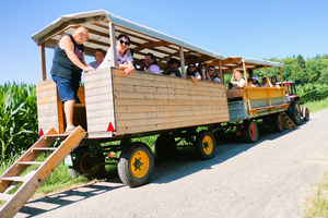 Eine Gruppe von Menschen sitzt in einem Holzwagen auf einem Feldweg.