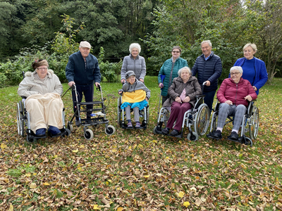 Gruppe von acht Menschen in Rollstühlen, umgeben von herbstlichen Laub.