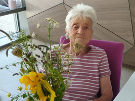 Eine ältere Frau sitzt mit einem bunten Blumenstrauß in der Hand.