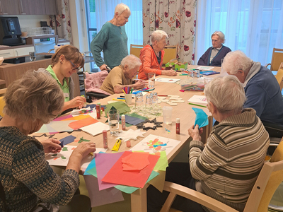 Ältere Menschen basteln gemeinsam an einem Tisch mit buntem Papier und Materialien.