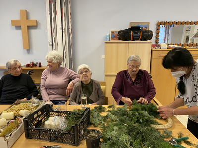 Ältere Menschen gestalten gemeinsam einen Adventskranz in einem gemütlichen Raum.