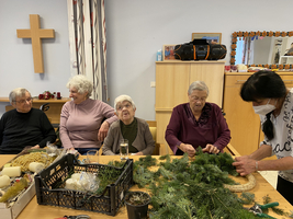 Ältere Menschen gestalten gemeinsam einen Adventskranz in einem gemütlichen Raum.