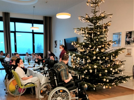 Weihnachtsfeier mit einem schön dekorierten Baum und mehreren Gästen in Rollstühlen.