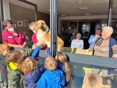 Kinder interagieren mit einem hundeartigen Tier durch ein offenes Fenster.