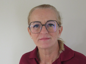Eine Frau mit Brille trägt ein rotes Poloshirt und steht vor einer neutralen Wand.