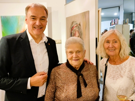 Drei Personen posieren lächelnd vor einer Kunstinstallation in einem modernen Raum.