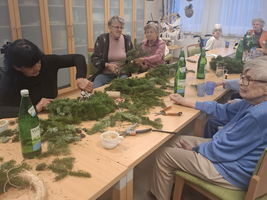Frauen basteln gemeinsam mit Tannenzweigen an einem Tisch.