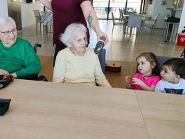 Drei ältere Frauen und zwei Kinder sitzen am Tisch in einem freundlichen Raum.
