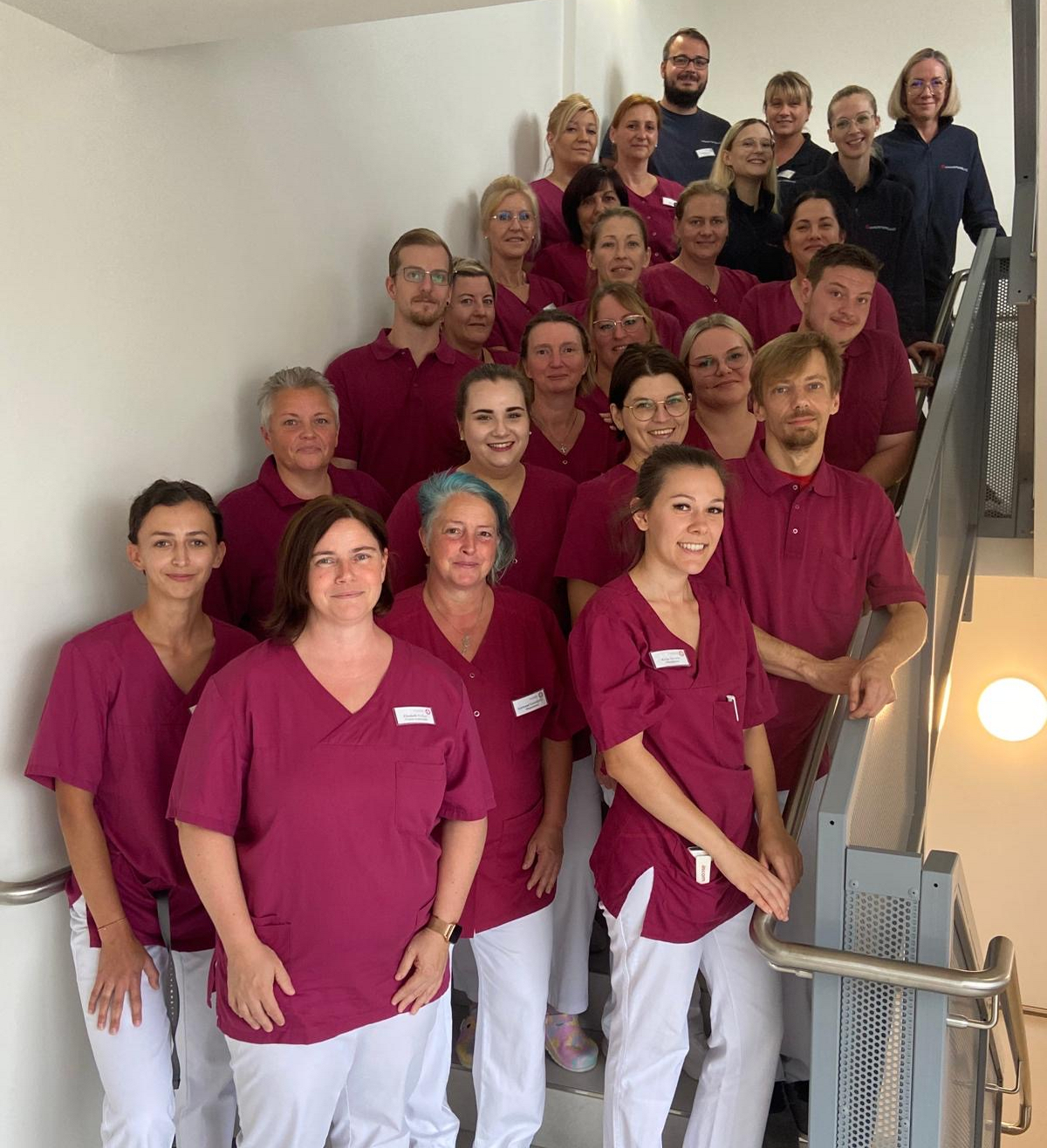 Gruppenfoto von Pflegekräften auf einer Treppe, alle tragen rote und weiße Kleidung.