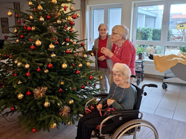 Drei Frauen dekorieren einen Weihnachtsbaum in einem Raum für Senioren.