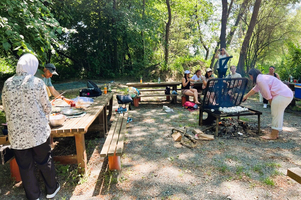 Gruppe von Menschen beim Grillen in einem schattigen, grünen Park.