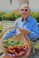 Ein älterer Mann sitzt auf einer Bank und hält einen Korb mit Rosen.