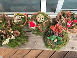 Fünf dekorierte Adventskränze mit Moos und verschiedenen Ornamenten.