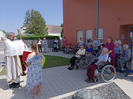 Ein Priester segnet eine Gruppe von Senioren und Kindern im Freien.