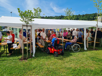 Menschen stehen und sitzen unter einem Zelt bei einer Veranstaltung im Freien.