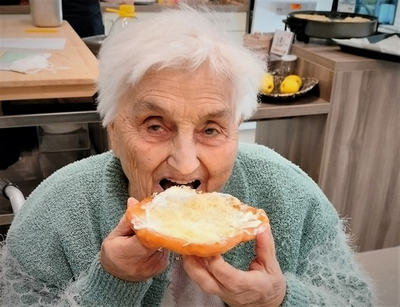 Eine ältere Frau lächelt und hält ein belegtes Brötchen in der Hand.